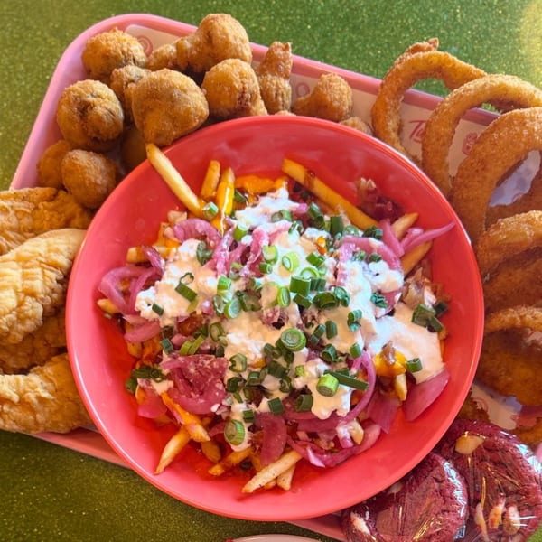 A pink tray filled with American appetizers: loaded fries, fried mushrooms, onion rings, and chicken tenders.