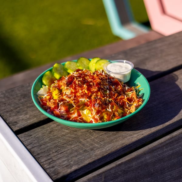 A BBQ chicken salad with pickles and ranch dressing in a green bowl on a wooden table.