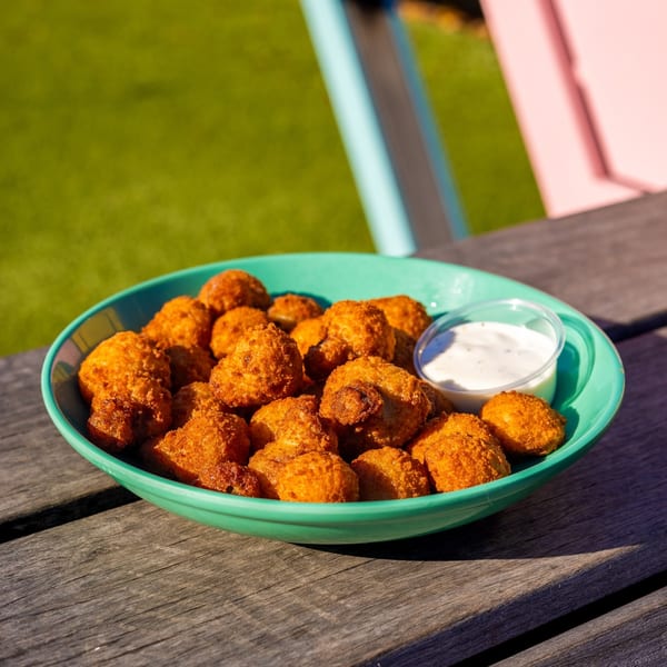 A teal bowl of crispy fried mushrooms and a side of ranch dressing on a wooden table.