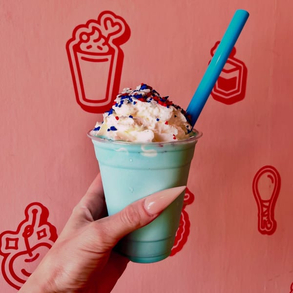 Hand holding a blue milkshake with whipped cream and red, white, and blue sprinkles.