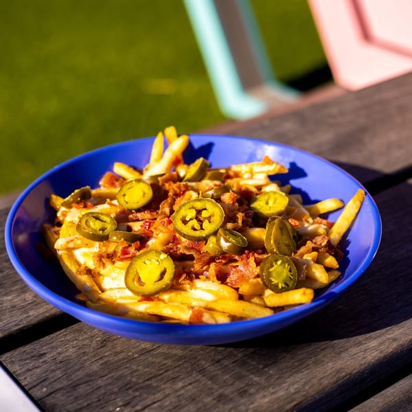 Baby's loaded fries with melted cheese, bacon bits, and jalapeños in a blue bowl on a wooden table.
