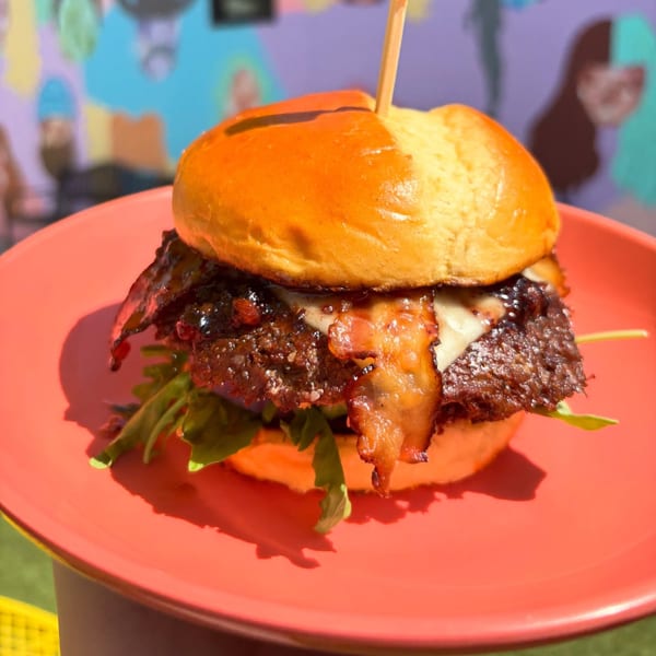 A Baby's burger with bacon, cheese, and arugula on a red plate, with a colorful background.